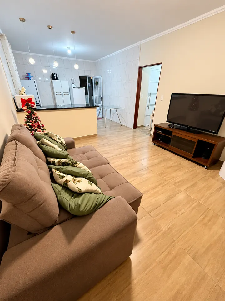 Sala com sofá e TV, com a cozinha ao fundo